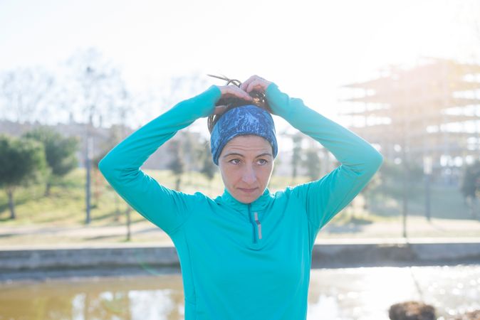 Woman in ear warmers adjusting hair while working out in park on sunny fall day