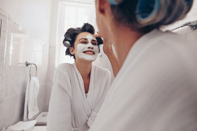 Smiling woman in bathrobe smiling while her mom applies face cream to her face at home