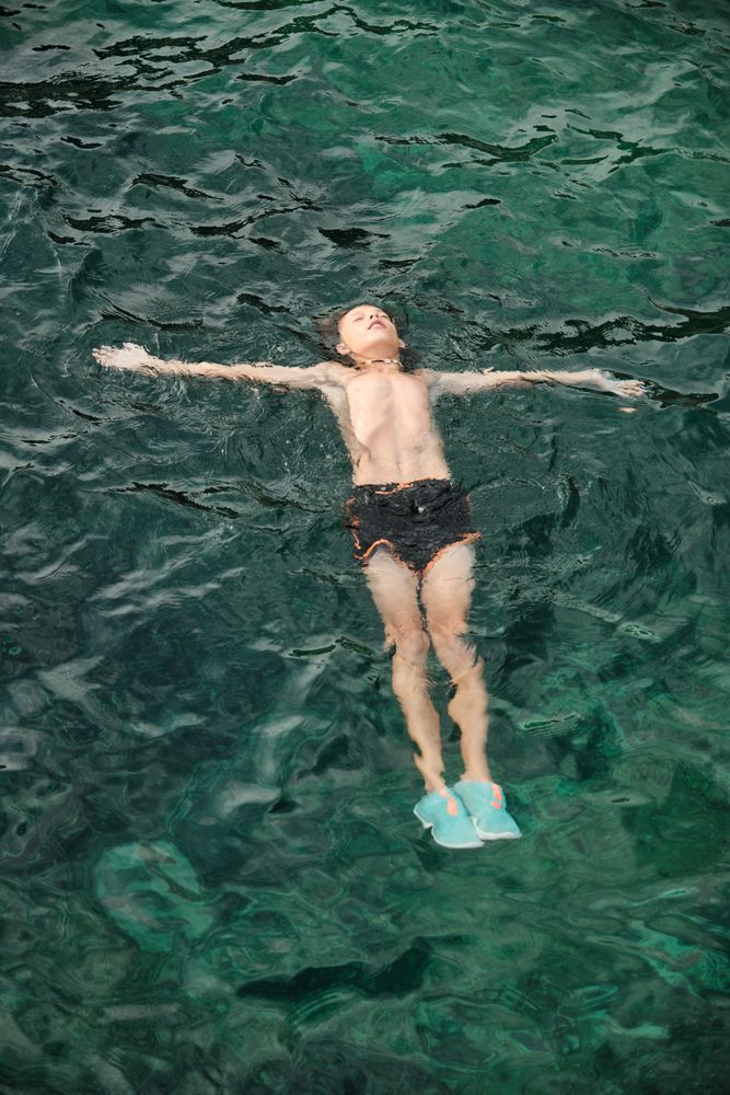 Shirtless boy floating and relaxing on sea water