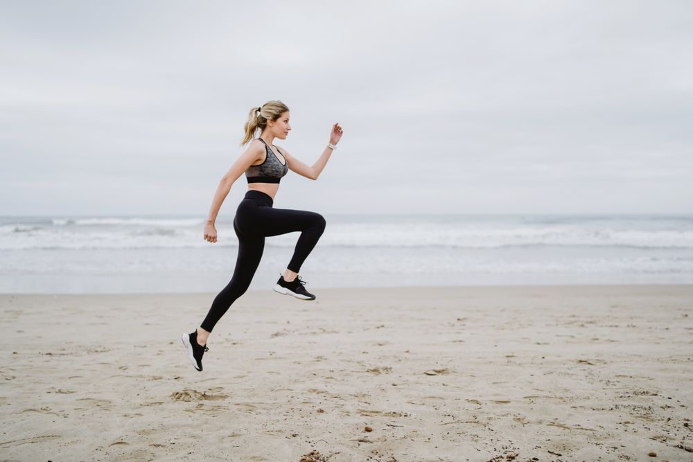 Young female athlete in active wear jogging while jumping at sea beach