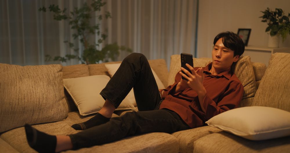 South Korean Young Man Enjoying His Leisure Time while Relaxing and Using a Smartphone.