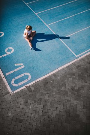 Woman sitting and stretching her legs at the beginning of an athletic track
