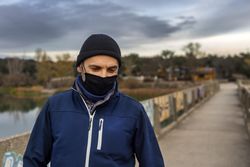 Man in dark knit cap and blue zip up hoodie standing on road