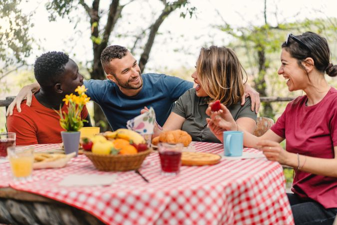 Group of multi-ethnic cheerful friends get together at farmhouse restaurant having fun eating fruits at brunch