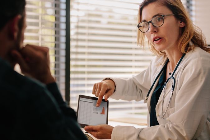 Confident female doctor talking with patient with test results on tablet
