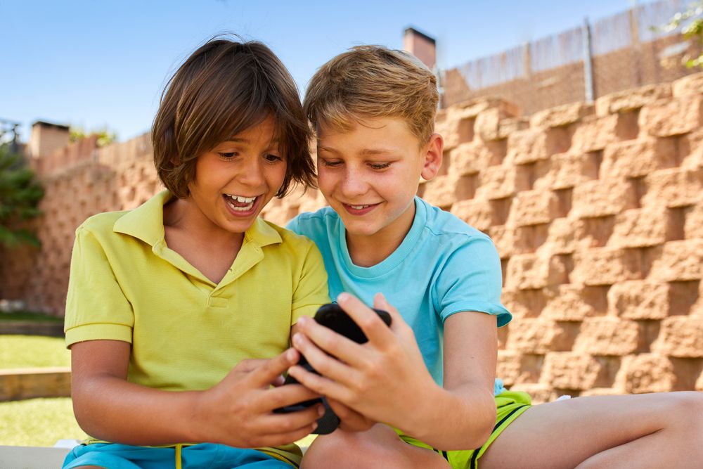 Cheerful boys browsing smartphone on sunbed