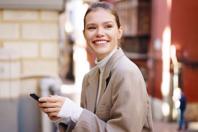 A Smiling Woman in a Stylish Outfit Holding Her Smartphone While Outdoors Enjoying Nature