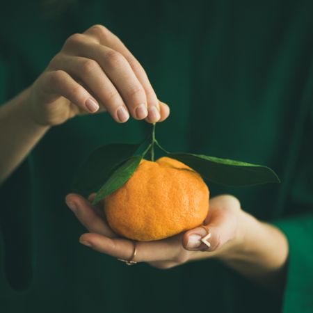 Woman in green holding tangerine, square crop