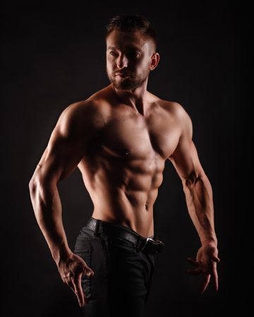 Bodybuilder competitor practicing upper body poses in dark studio