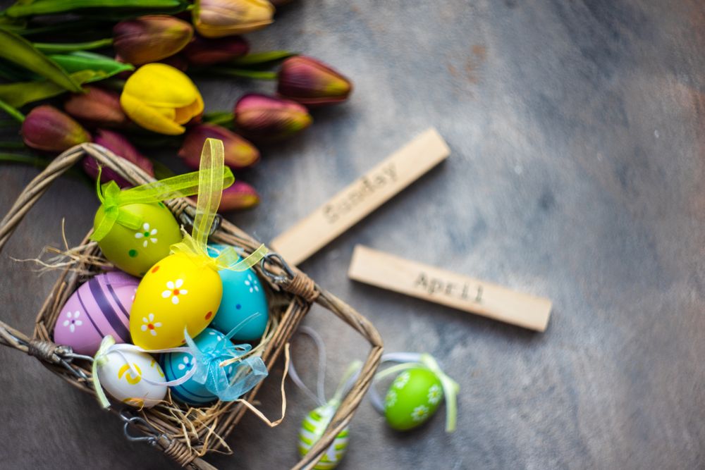 Top view of decorative Easter eggs in basket on table with tulips