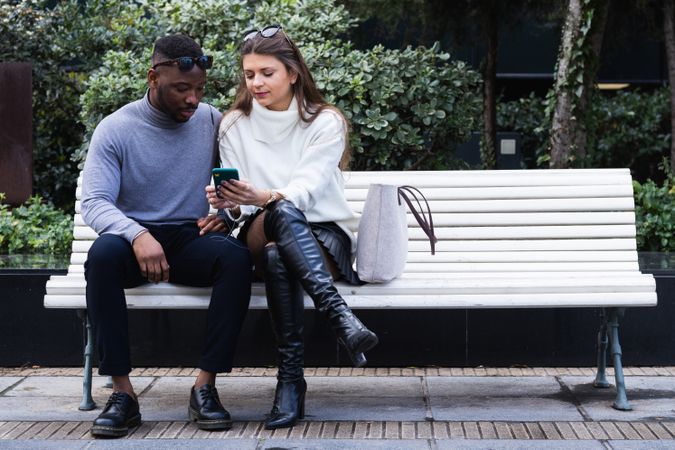 Joyful multiethnic couple listening music on smartphone in park