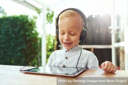 Smiling blond boy using headphones while watching show on digital tablet bDB7V5