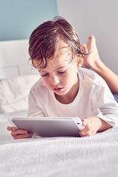Boy lying on bed and watching video on tablet