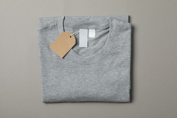 Folded blank gray t-shirt with tag on gray background, space for text