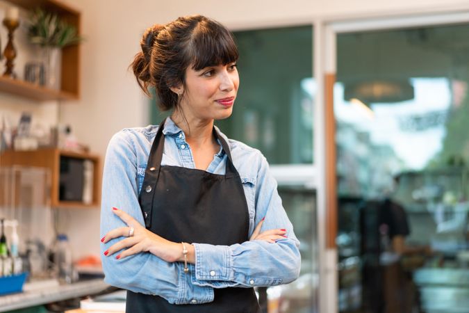 Woman wearing apron standing in cafe with arms crossed