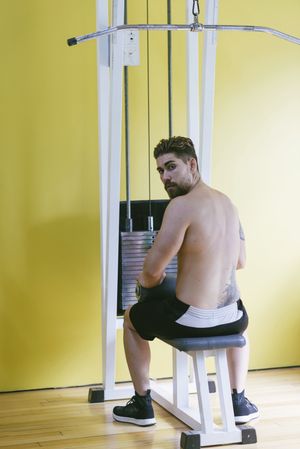 Fit man turning around while sitting on lat pull down machine