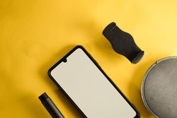 Phone with mockup screen and accessories on yellow table with copy space