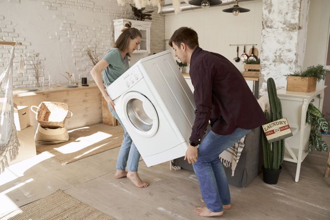 Enthusiastic couple carrying washing machine into new kitchen