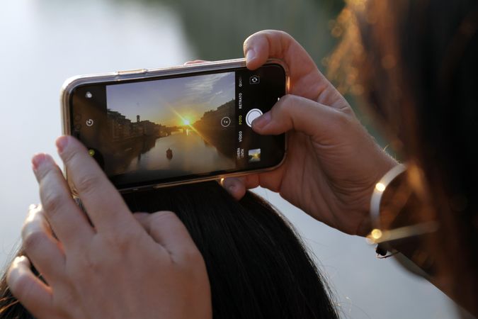 Person holding smartphone taking photo of sunset