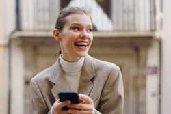 Joyful Young Woman Enthusiastically Engaging with Her Smartphone in a Bustling Urban Setting