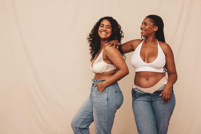 Two women smiling and having fun in studio wearing denim jeans and bras