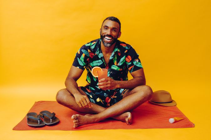 Black male sitting on towel and laughing while holding tropical drink