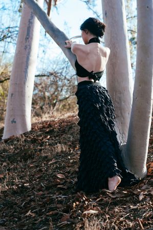 Back view of model with open backed shirt and formal skirt reaching out to a tree outside