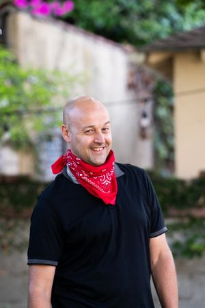 Portrait of man smiling and looking at camera standing outside wearing red bandana around his neck