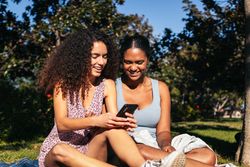Black Latina friends using a smartphone in the park.