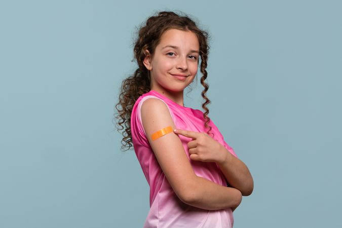 Girl pointing at orange bandage on arm after vaccination