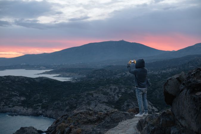 Male taking photo on cliff at dusk