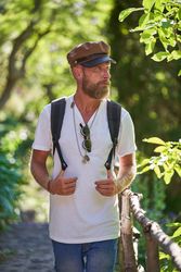 Traveling bearded man in cap walking in forest