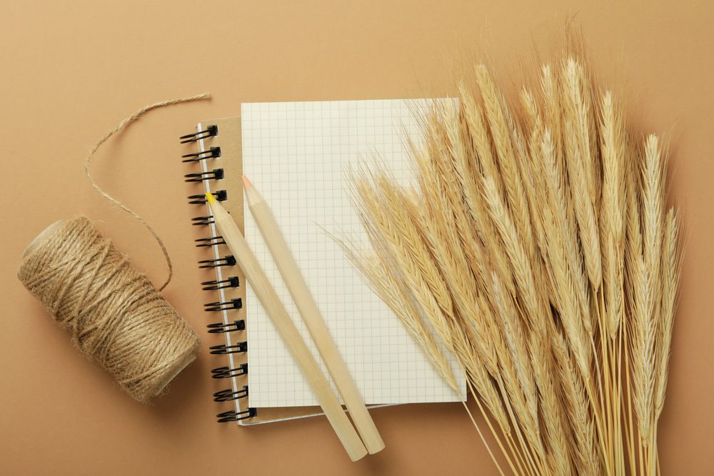 Notebook with dried flowers, yarn, pencils on neutral brown background