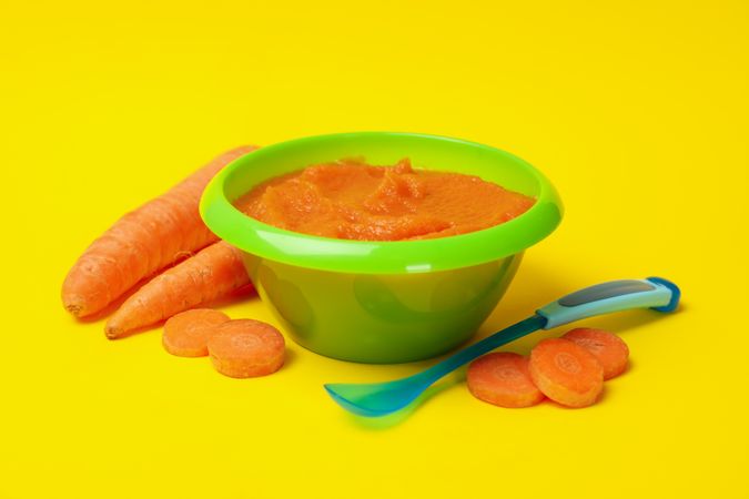 Bowl with vegetable puree on yellow background. Baby food