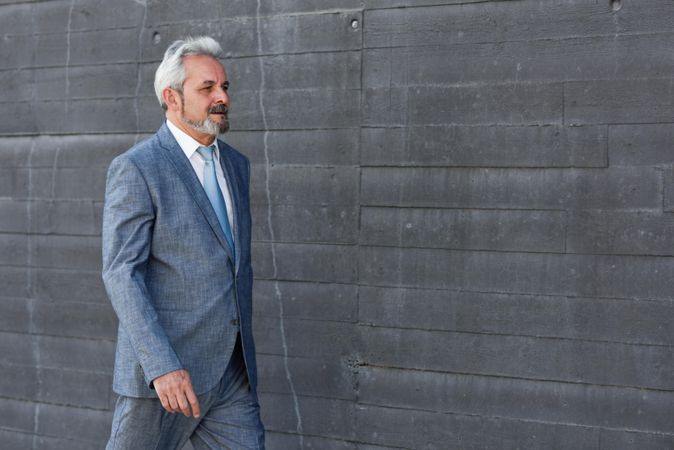 Business man wearing suit and walking next to concrete grey wall, with copy space