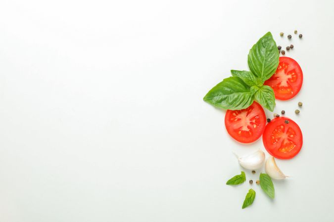 Flat lay composition with fresh cherry tomatoes slices with basil, pepper and garlic on plain background, space for text and top view. Ripe vegetables