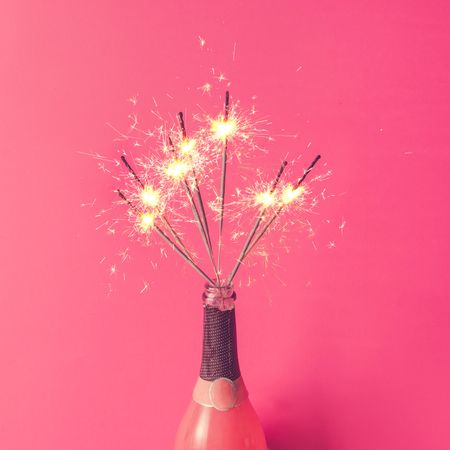 Champagne bottle with sparklers on pink background