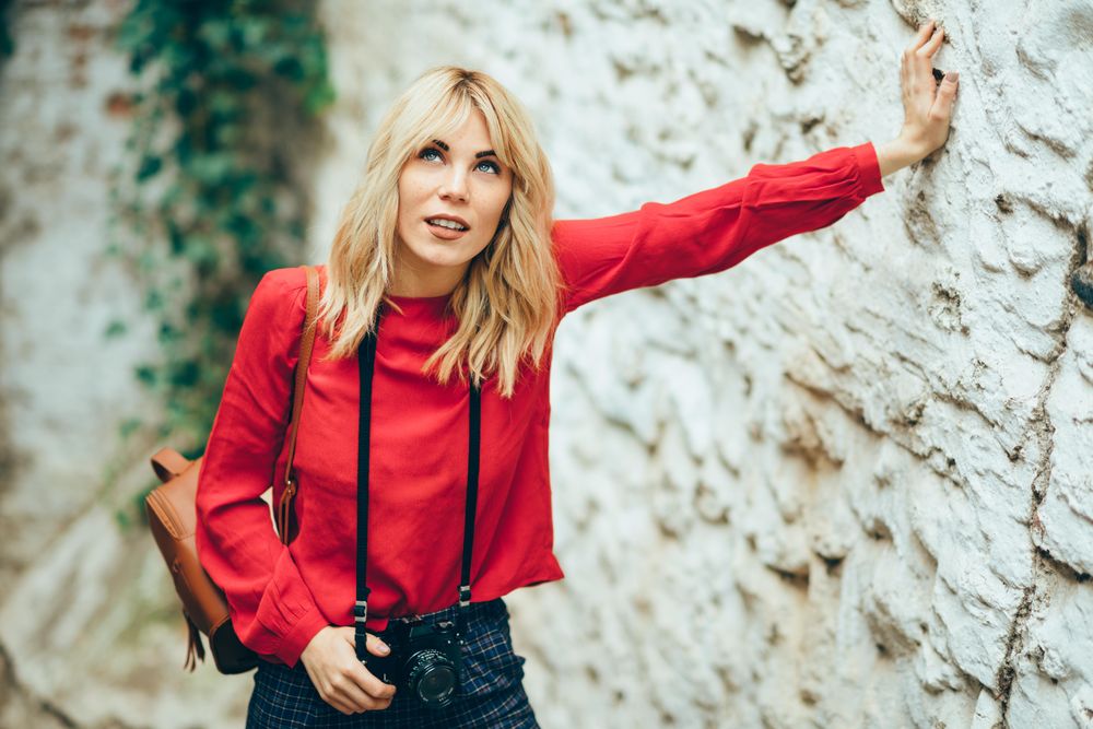 Curious photographer in red sweater walking around European town with camera