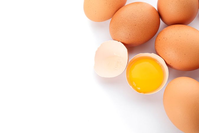 Chicken eggs and half broken egg with yolk  isolated on light background, closeup and top view