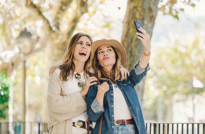Smiling women taking selfie in street near cute tree