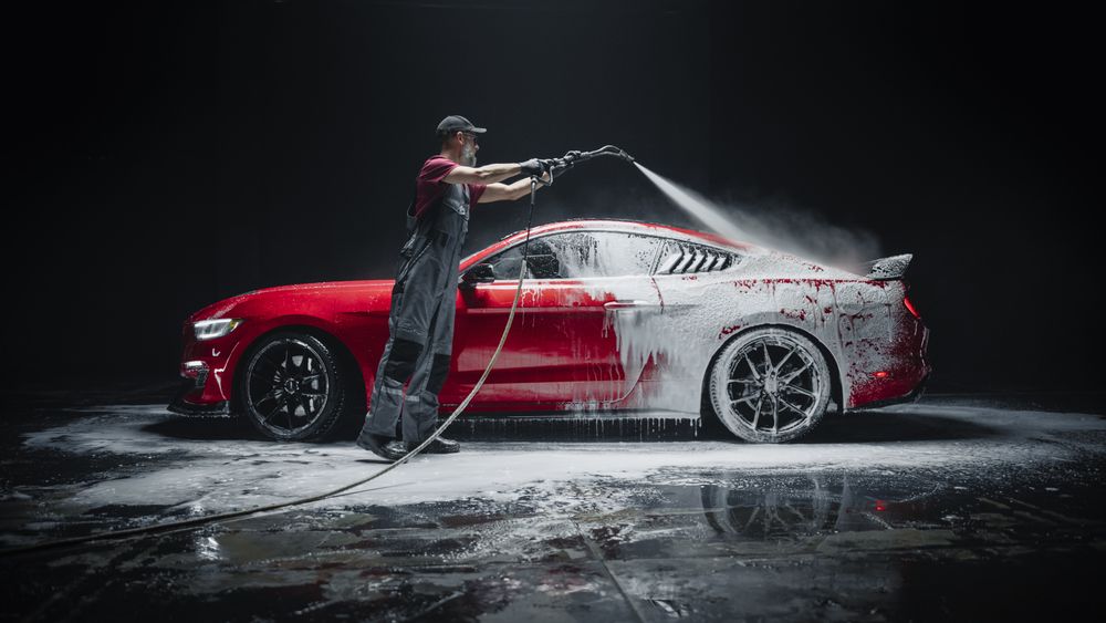 Automotive Detailer Washing Away Smart Soap and Foam with a Water High Pressure Washer.