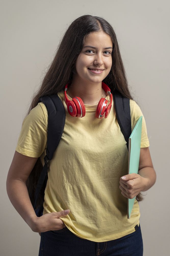 Smiling teenage girl with backpack and headphones holding a folder in casual studio portrait