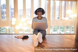 Woman sitting on floor smiling and working on her laptop on second story beekAb