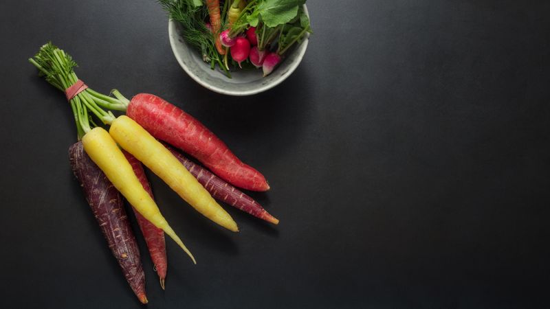 Colorful carrots and radishes bunched together on table alongside a bowl dill leaves