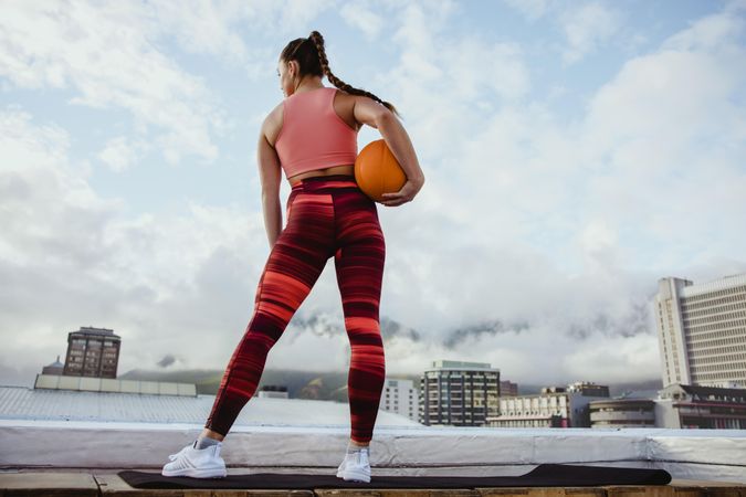 Fit woman holding orange ball while working out on rooftop