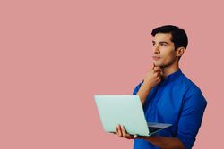 Contemplative Latino man holding laptop in pink room