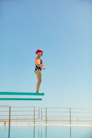 Girl preparing to jump off a diving board against clear blue sky