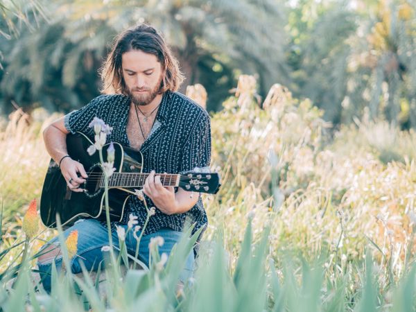 Hipster man in meadow with guitar