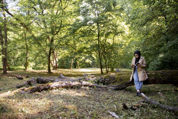 Woman in headscarf reading in a park leaning against a fallen tree
