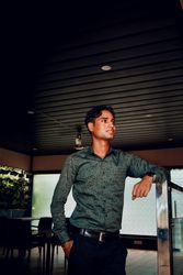 Man in gray dress shirt and dark pants standing indoor looking away